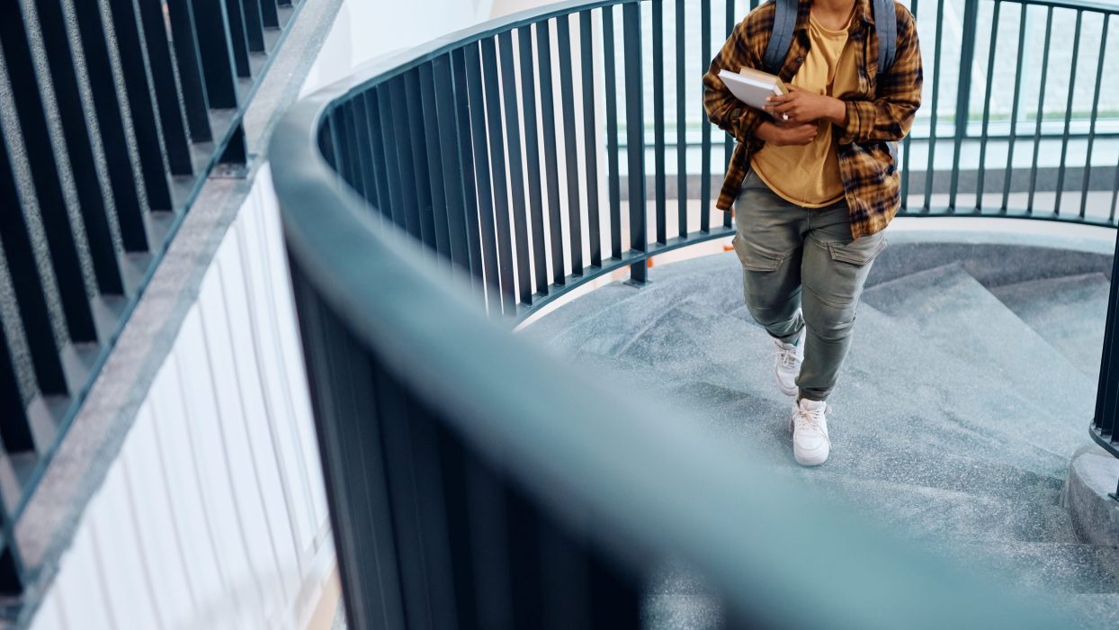 Happy African American student walking up the stairs at university hallway.